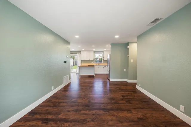a view of a kitchen and an empty room with wooden floor