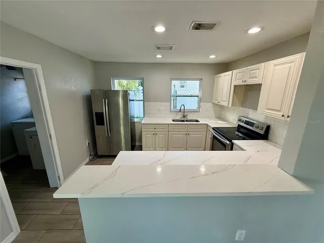 a large kitchen with stainless steel appliances a refrigerator a sink dishwasher a stove and white cabinets