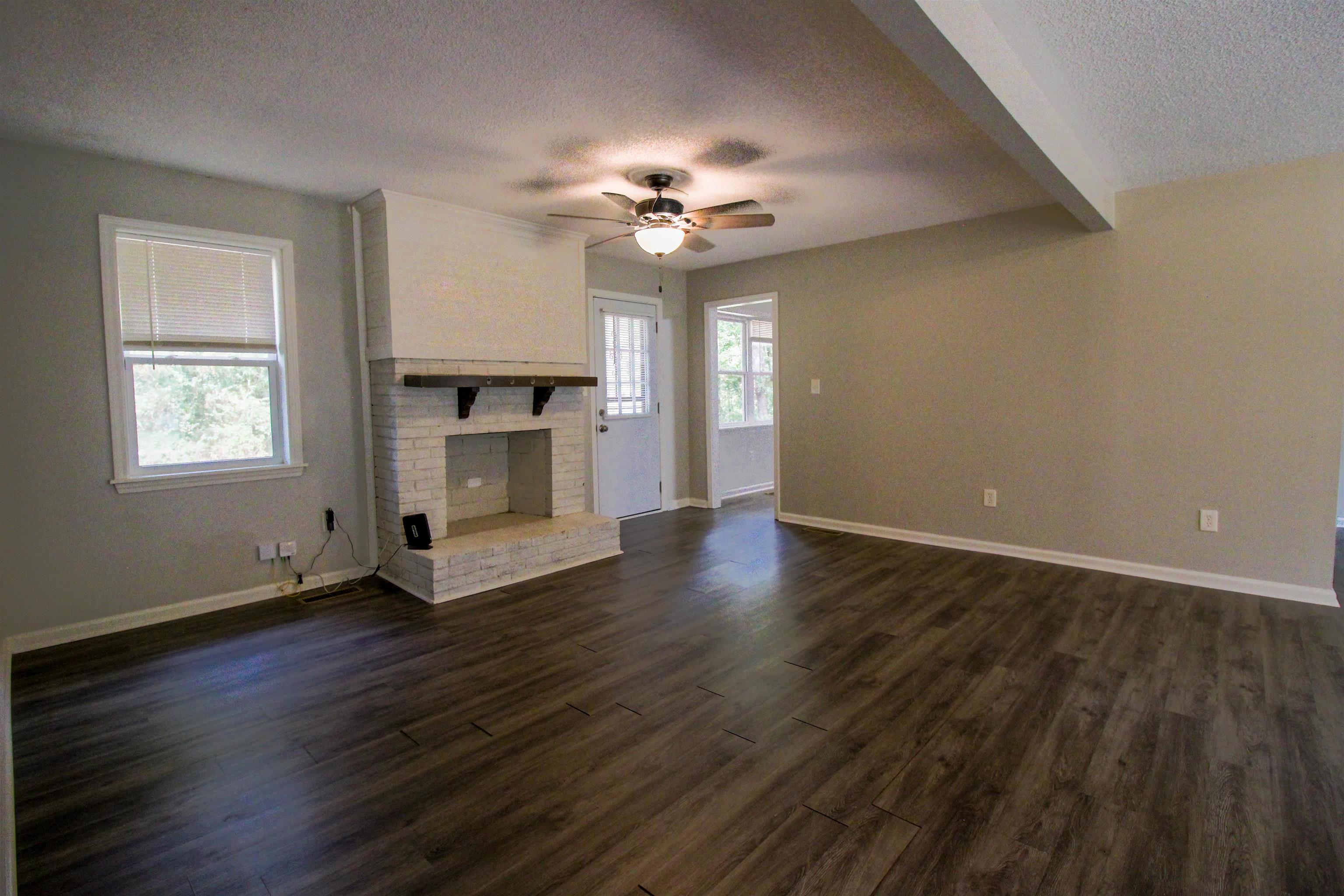 2089 Ralph Road Covington, TN 38019 - Photo 2 of 28 Living room featuring a textured ceiling, dark wood-style floors, a brick fireplace, a ceiling fan, and beamed ceiling.