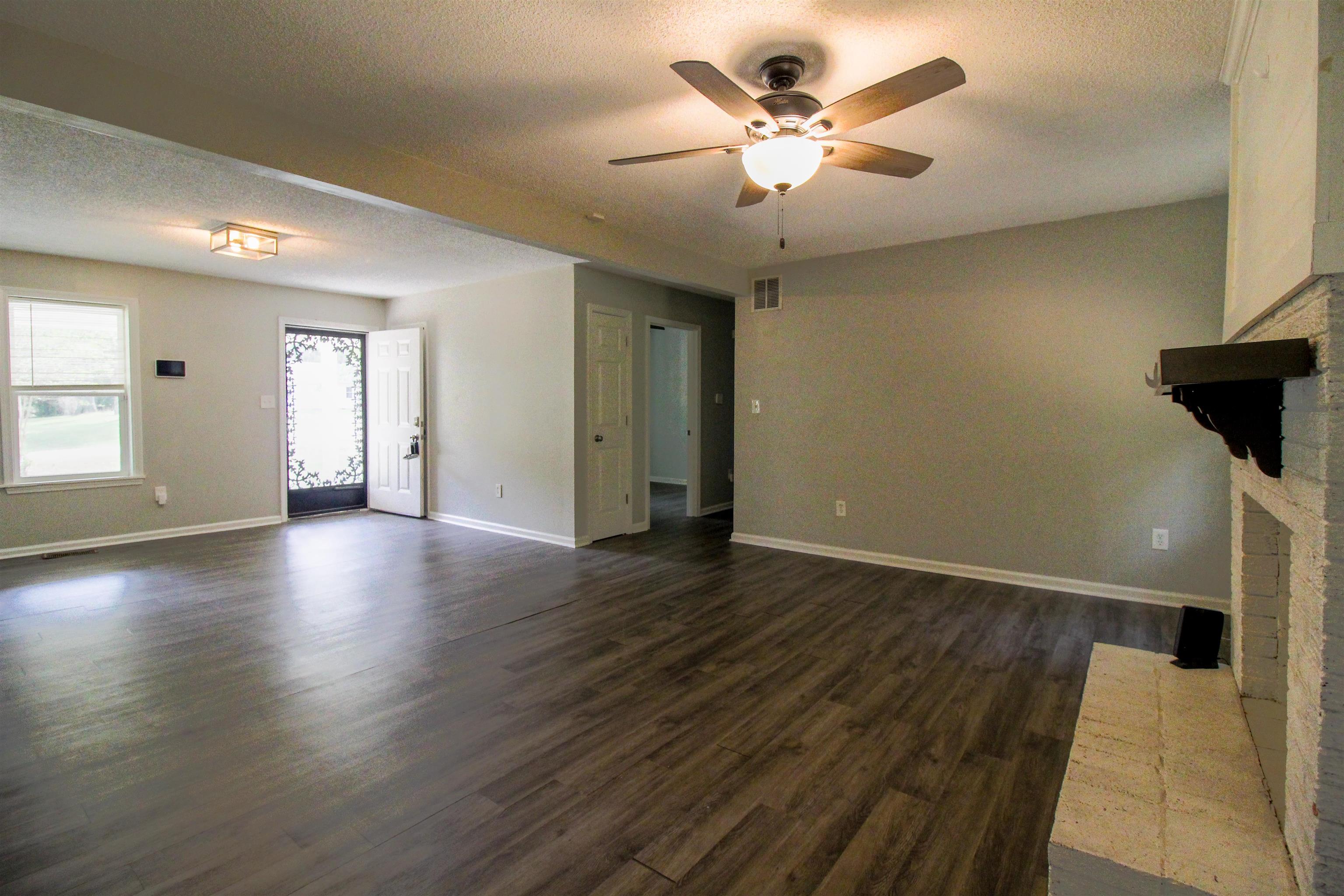 2089 Ralph Road Covington, TN 38019 - Photo 3 of 28 Living room featuring a textured ceiling, dark wood-style floors, a brick fireplace, a ceiling fan, and beamed ceiling.