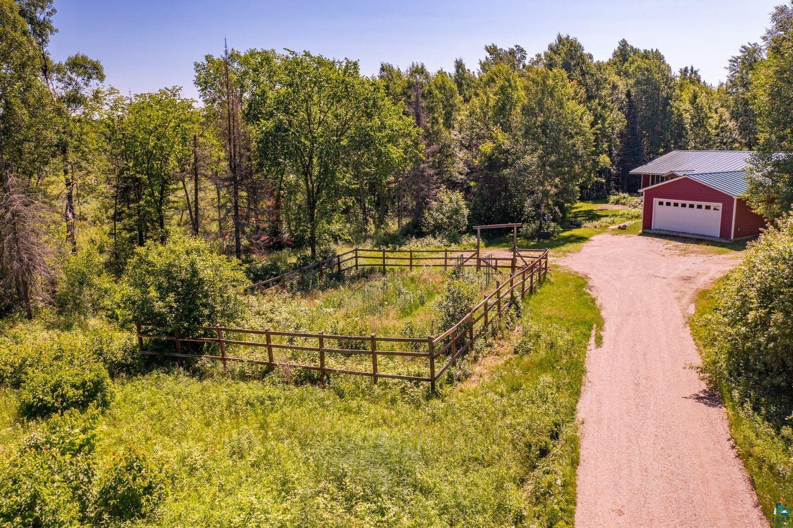 9734 Alango Road Angora, MN 55703 - Photo 29 of 41 Gravel driveway leading to a red-sided structure with a white garage door, set amidst abundant greenery and mature trees