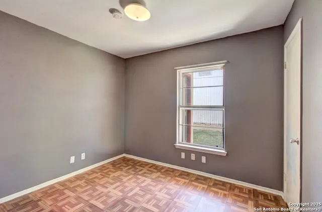 a view of an empty room with window and wooden floor