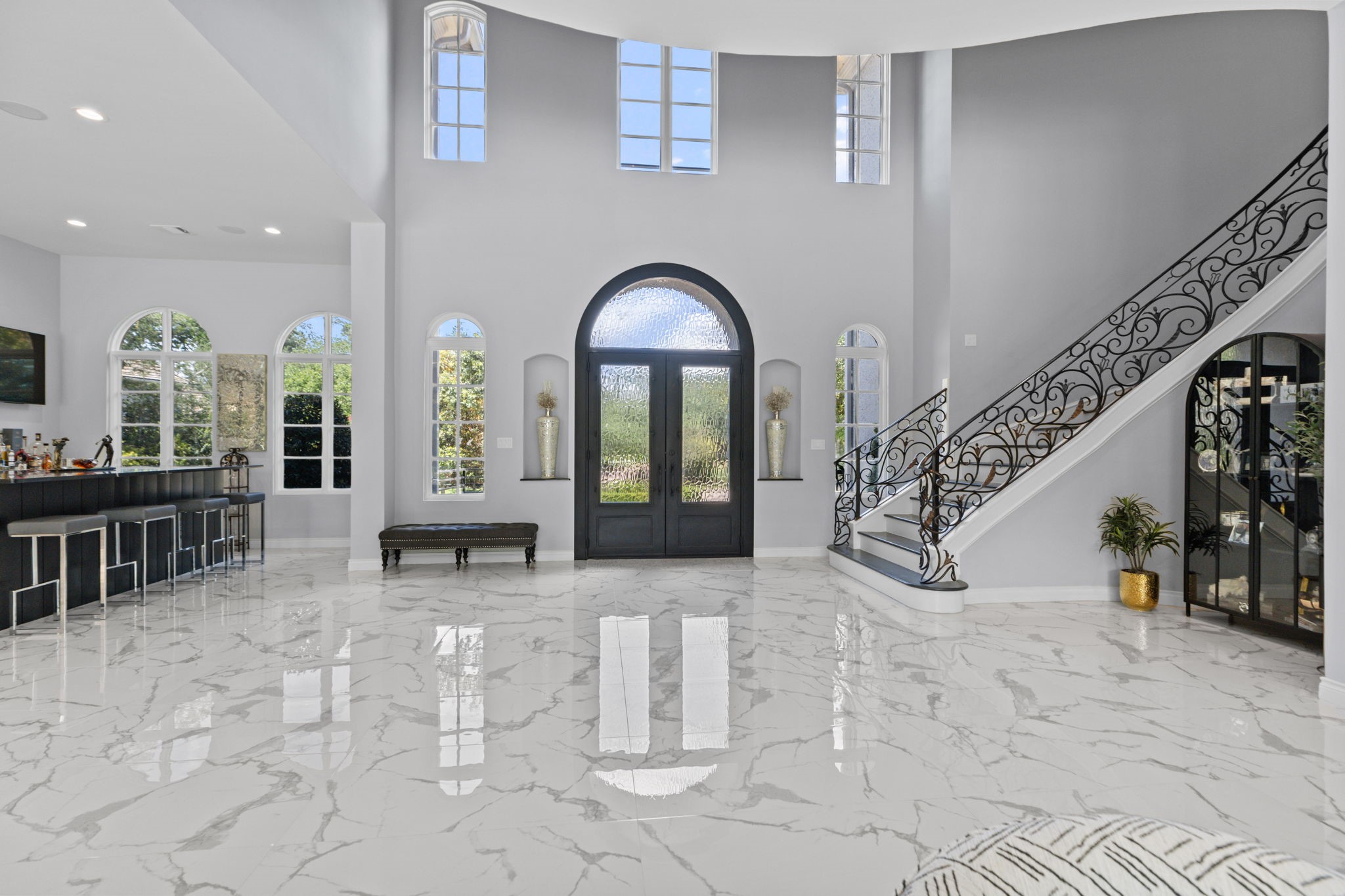 39 Maymont Way Spring, TX 77382 - Photo 5 of 50 This elegant entryway features high ceilings, large arched windows, and a sweeping staircase with ornate railings. The space is filled with natural light and has a polished marble floor. A stylish bar area and contemporary decor add to its luxurious feel.