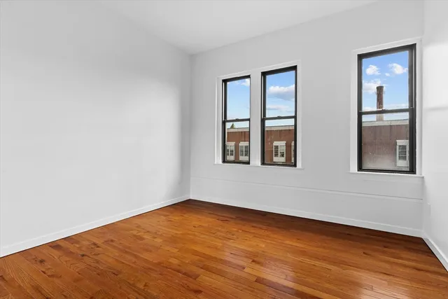 a view of an empty room with wooden floor and windows