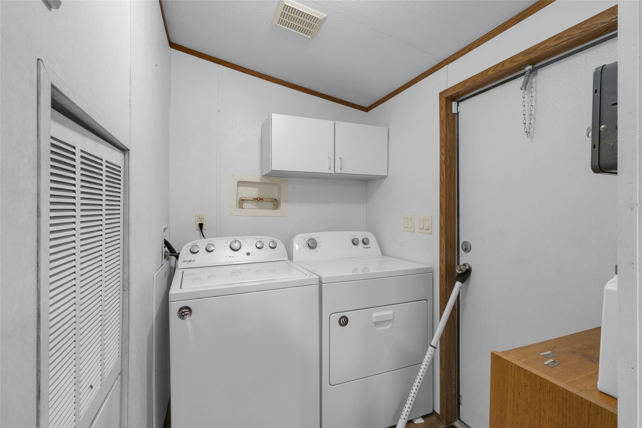 22094 Spear Road Porter, TX 77365 - Photo 34 of 45 This photo shows a compact laundry room equipped with a washer and dryer. It features overhead storage cabinets and a door leading outside, with white walls and wood trim providing a clean, functional space.