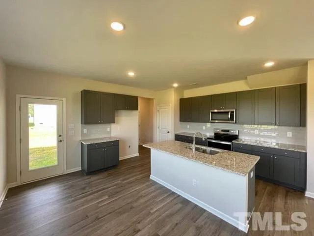 a large kitchen with stainless steel appliances a large counter top a stove a sink cabinets and a wooden floor
