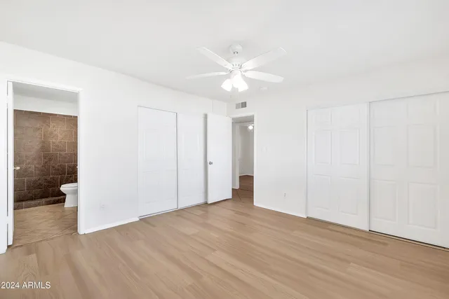 a view of an empty room with wooden floor and a ceiling fan