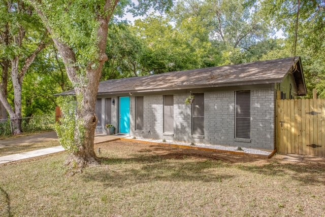 1109 Gardner Cove Austin, TX 78721 - Photo 2 of 13 A vibrant turquoise door welcomes you to this cozy home, nestled among mature trees on a lush green lawn.