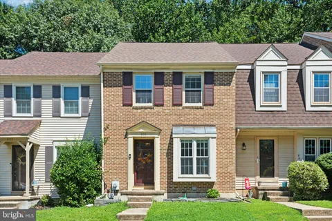 a view of a white house with a small yard and large trees