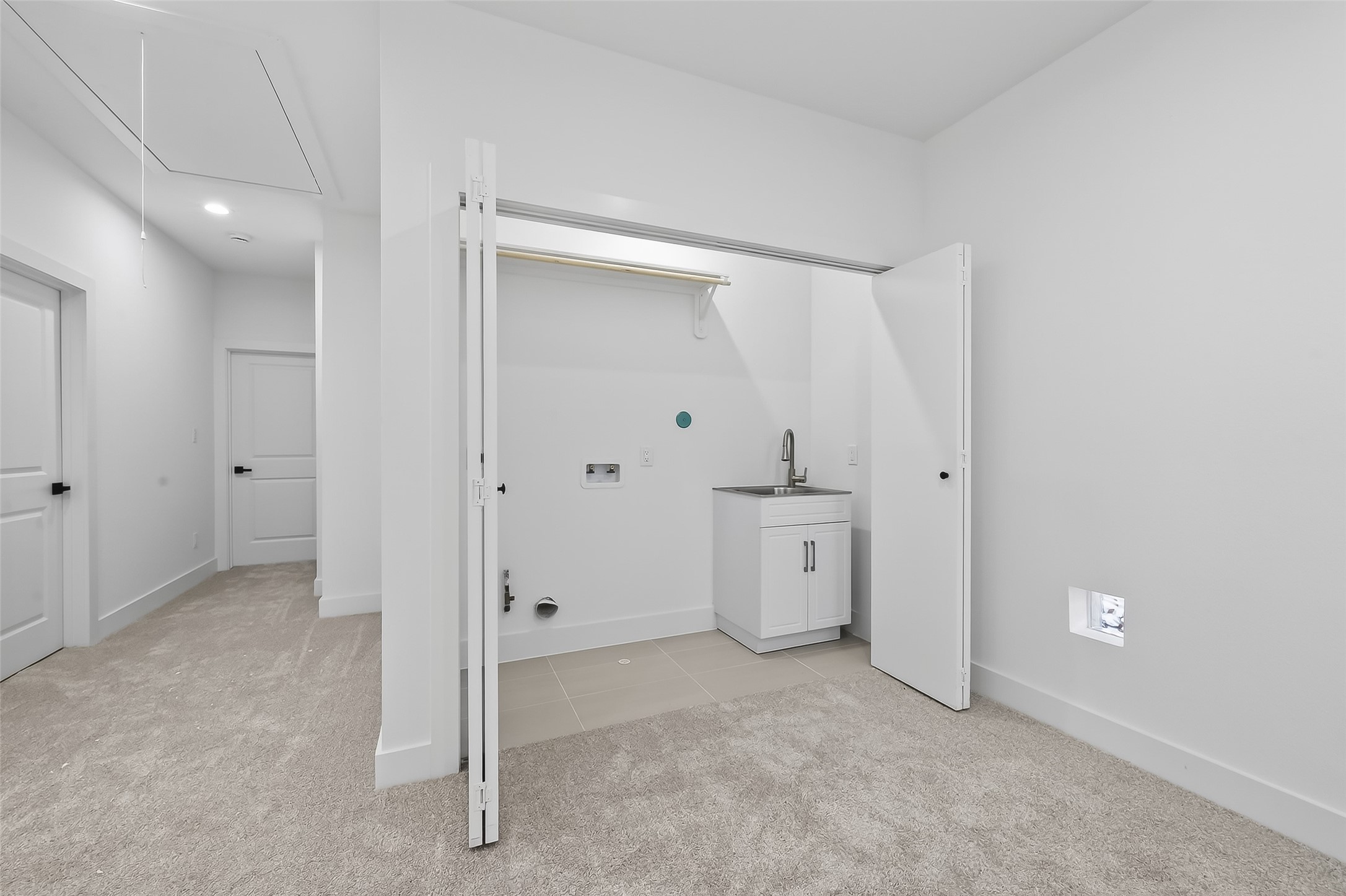 3514 Good Hope Street, Unit B Houston, TX 77021 - Photo 13 of 26 This photo shows a bright, laundry room with fresh white walls and carpeted flooring. It features a utility sink, washer/dryer hookups, and a storage shelf. The space is well-lit and adjacent to a hallway, providing easy access.