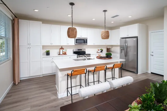 a kitchen with stainless steel appliances kitchen island granite countertop a refrigerator a stove and white cabinets with wooden floor