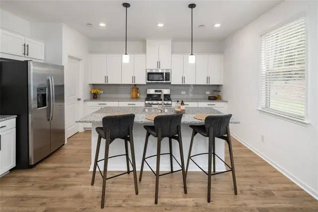 a kitchen with stainless steel appliances granite countertop a dining table chairs refrigerator and microwave