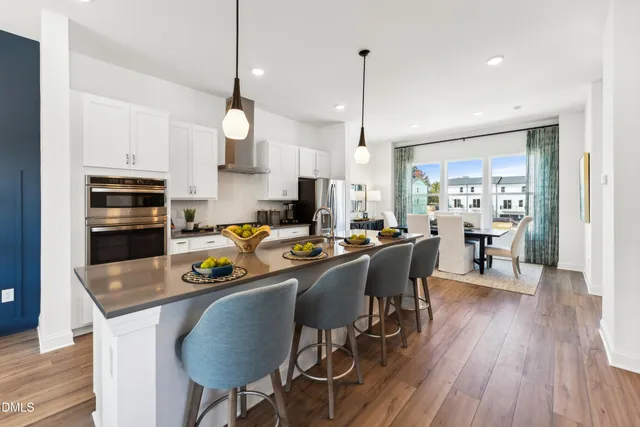 a kitchen with stainless steel appliances granite countertop a stove a refrigerator a kitchen island a dining table and chairs with wooden floor