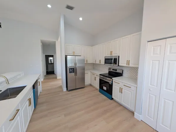 a view of an empty room and a kitchen with wooden floor and kitchen space