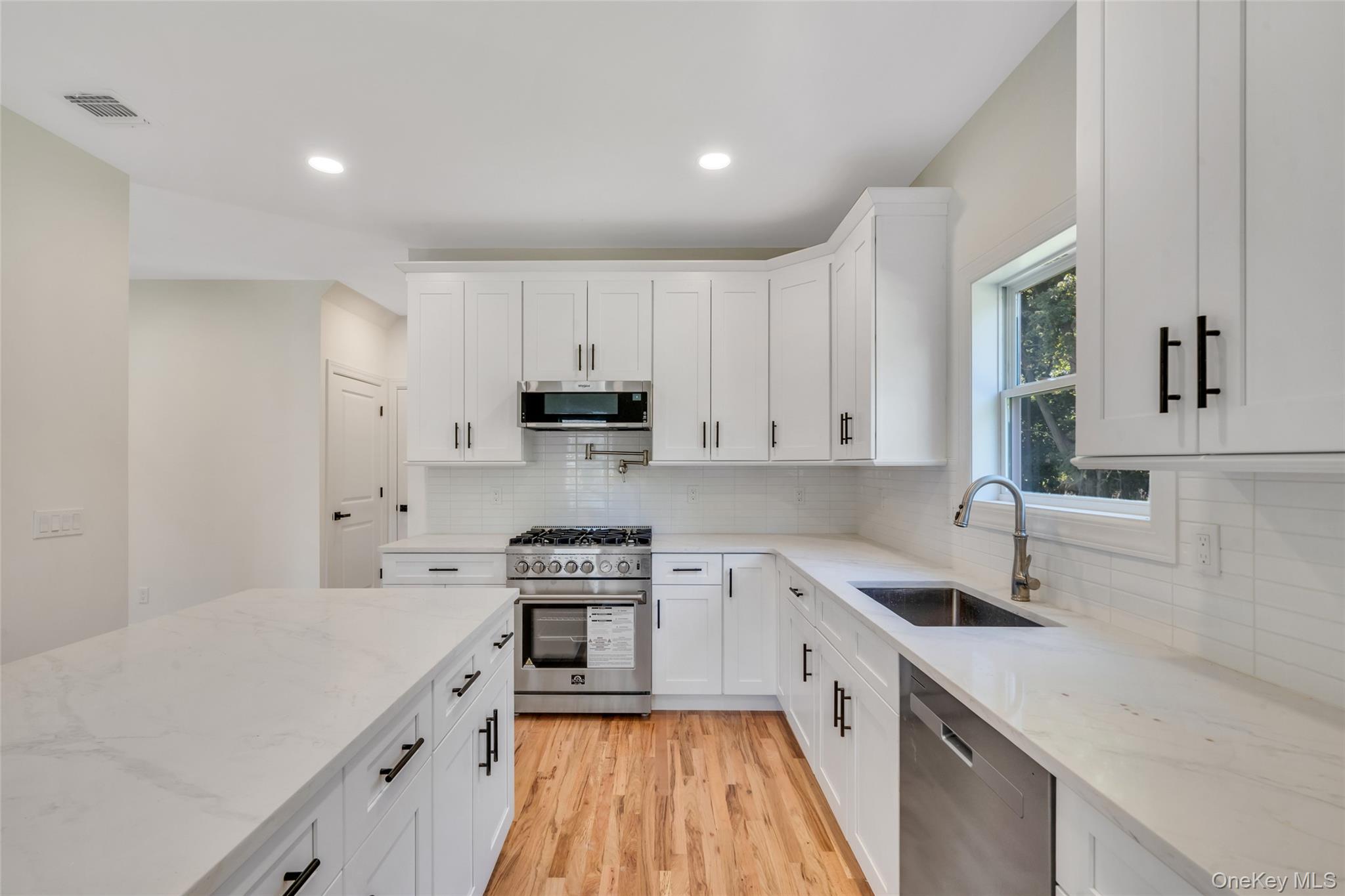 817 Pond View Road Riverhead, NY 11901 - Photo 21 of 36 a kitchen with stainless steel appliances a sink dishwasher a stove top oven a refrigerator with white cabinets and wooden floor
