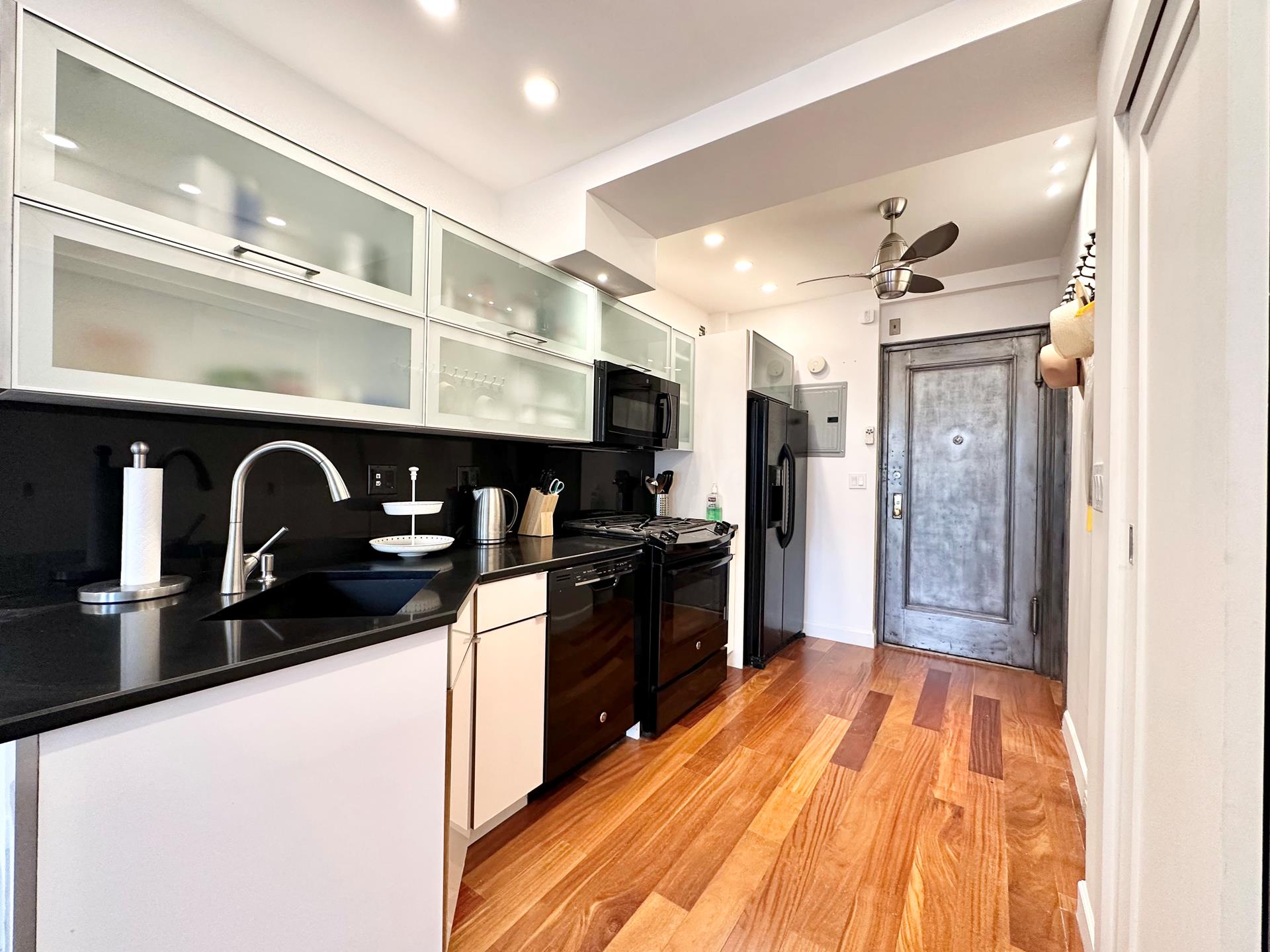 410 West 24th Street, Unit 15D Manhattan, NY 10011 - Photo 4 of 35 a kitchen with stainless steel appliances granite countertop a sink and wooden cabinets