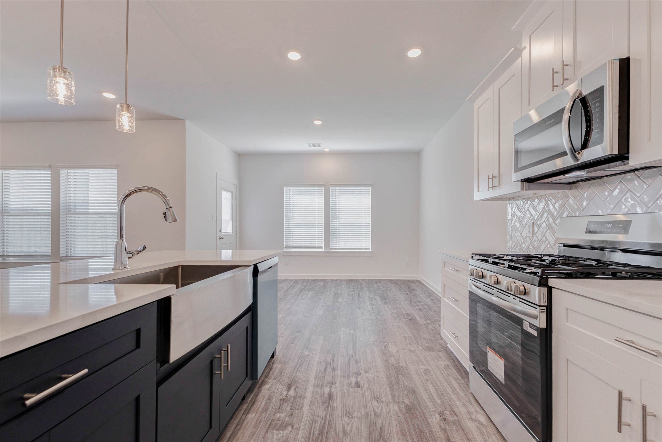 1038 Elsinore Drive Rosharon, TX 77583 - Photo 10 of 27 This perspective from the kitchen highlights the seamless open-concept design connecting the kitchen, dining, and living spaces. The oversized island with farmhouse sink provides generous prep space while overlooking the main living area, making it perfect for entertaining or everyday living. Stainless steel appliances, modern cabinetry, pendant lighting, and sleek quartz countertops create a bright and stylish kitchen environment that flows effortlessly into the spacious gathering areas beyond.