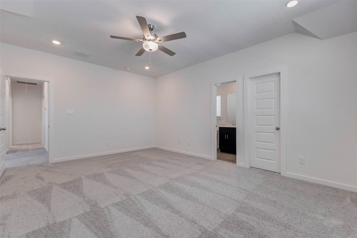 1038 Elsinore Drive Rosharon, TX 77583 - Photo 13 of 27 A second view of the primary suite highlights the generous layout and thoughtful design. The room easily accommodates large furniture while still offering ample open floor space. The en-suite bathroom entry is conveniently positioned for privacy, and the neutral finishes create a calming atmosphere that can easily adapt to any personal style or décor preferences.