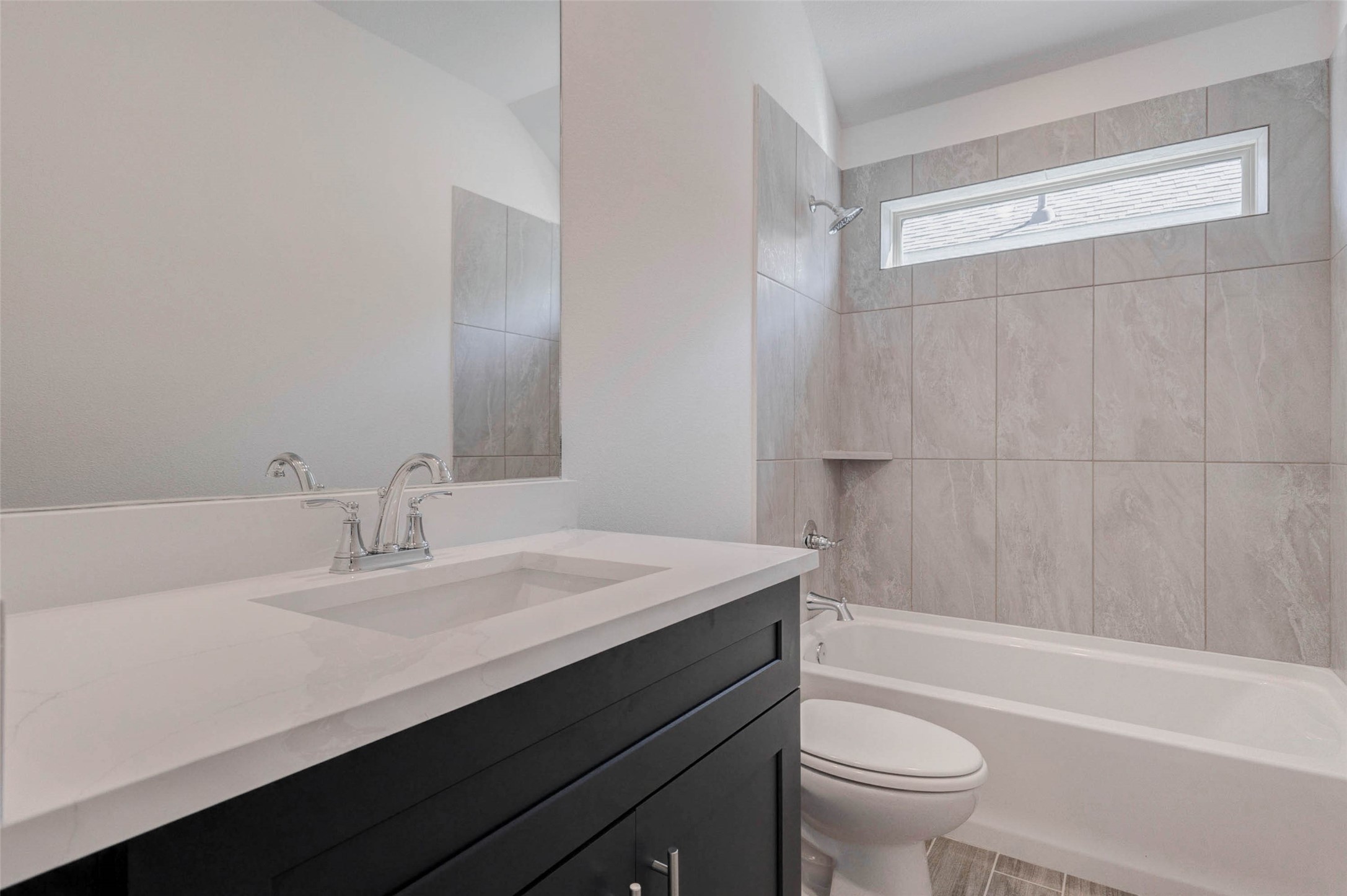 1038 Elsinore Drive Rosharon, TX 77583 - Photo 17 of 27 This stylish bathroom showcases modern finishes including a sleek vanity with quartz countertop, contemporary fixtures, and a spacious tub and shower combination with tile surround. A large mirror enhances the sense of space while the window provides natural light and ventilation. Designed with both style and functionality in mind, this bathroom offers a clean and comfortable environment for daily routines.
