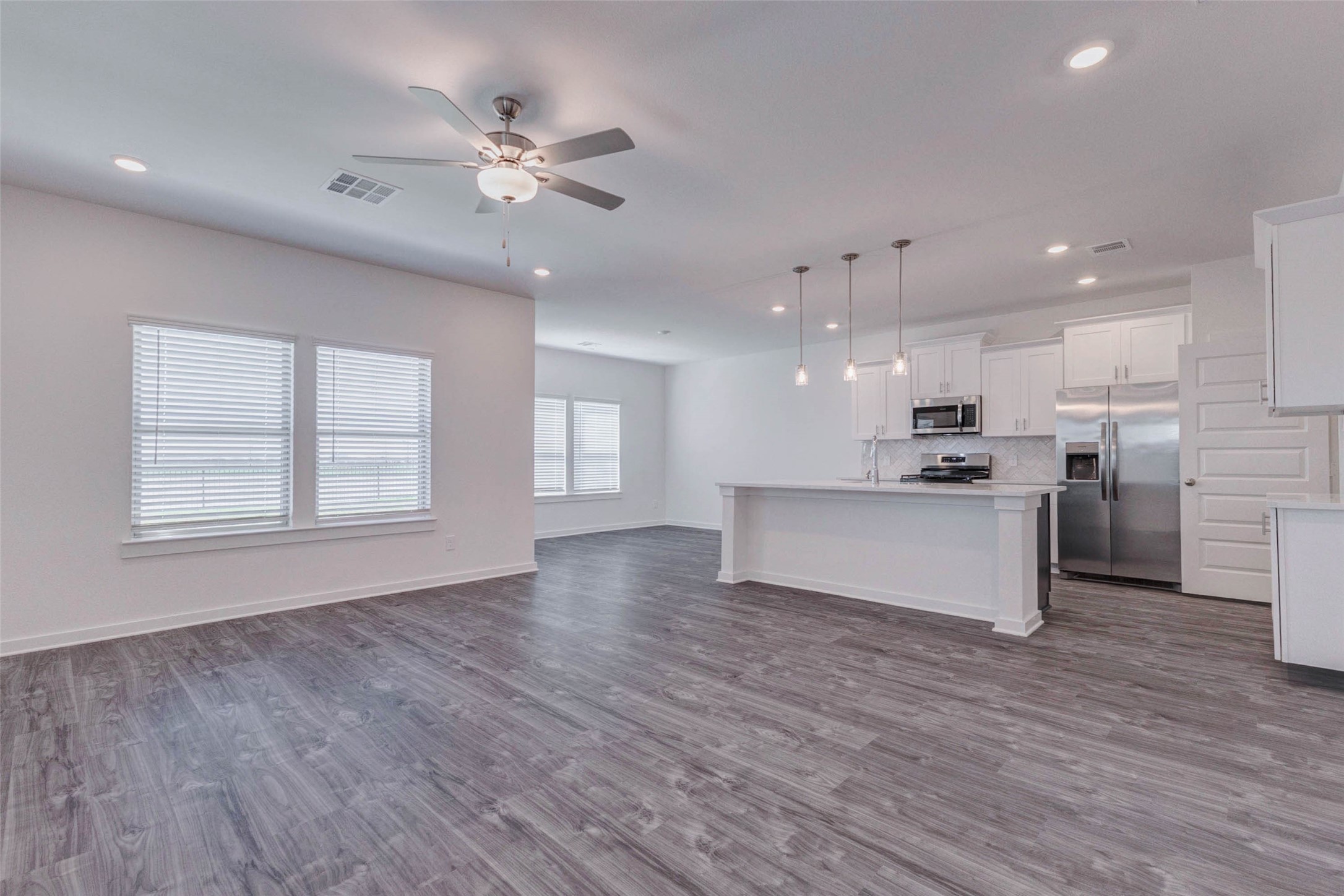 1038 Elsinore Drive Rosharon, TX 77583 - Photo 5 of 27 Step inside to an expansive open-concept living space filled with natural light and modern finishes. Wide-plank flooring flows seamlessly throughout the main area, creating a warm and cohesive feel. Large windows brighten the room, while recessed lighting and a ceiling fan add both comfort and functionality. The spacious layout provides plenty of room for relaxing, entertaining, and everyday living in a bright and welcoming environment.