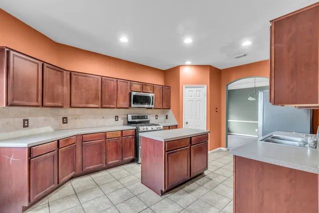 a kitchen with stainless steel appliances granite countertop a stove top oven a sink dishwasher and a refrigerator with wooden cabinets