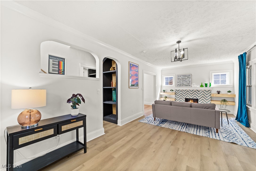 Living area featuring crown molding, built in shelves, light wood finished floors, a fireplace, and a textured ceiling