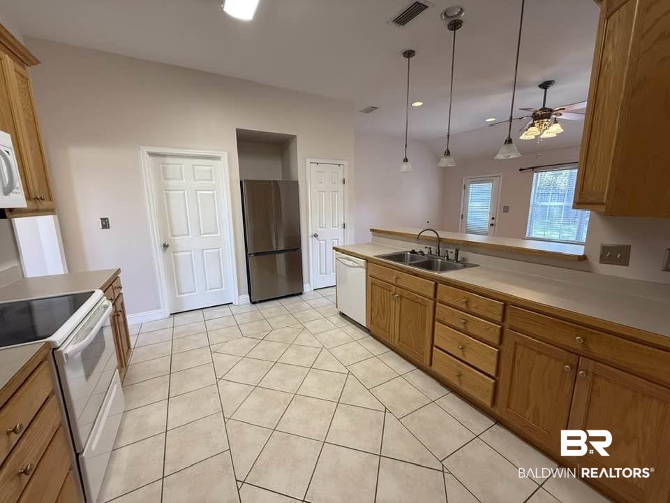 10428 South Side Loop Fairhope, AL 36532 - Photo 17 of 28 Kitchen with light tile patterned floors, visible vents, brown cabinetry, a sink, and white appliances