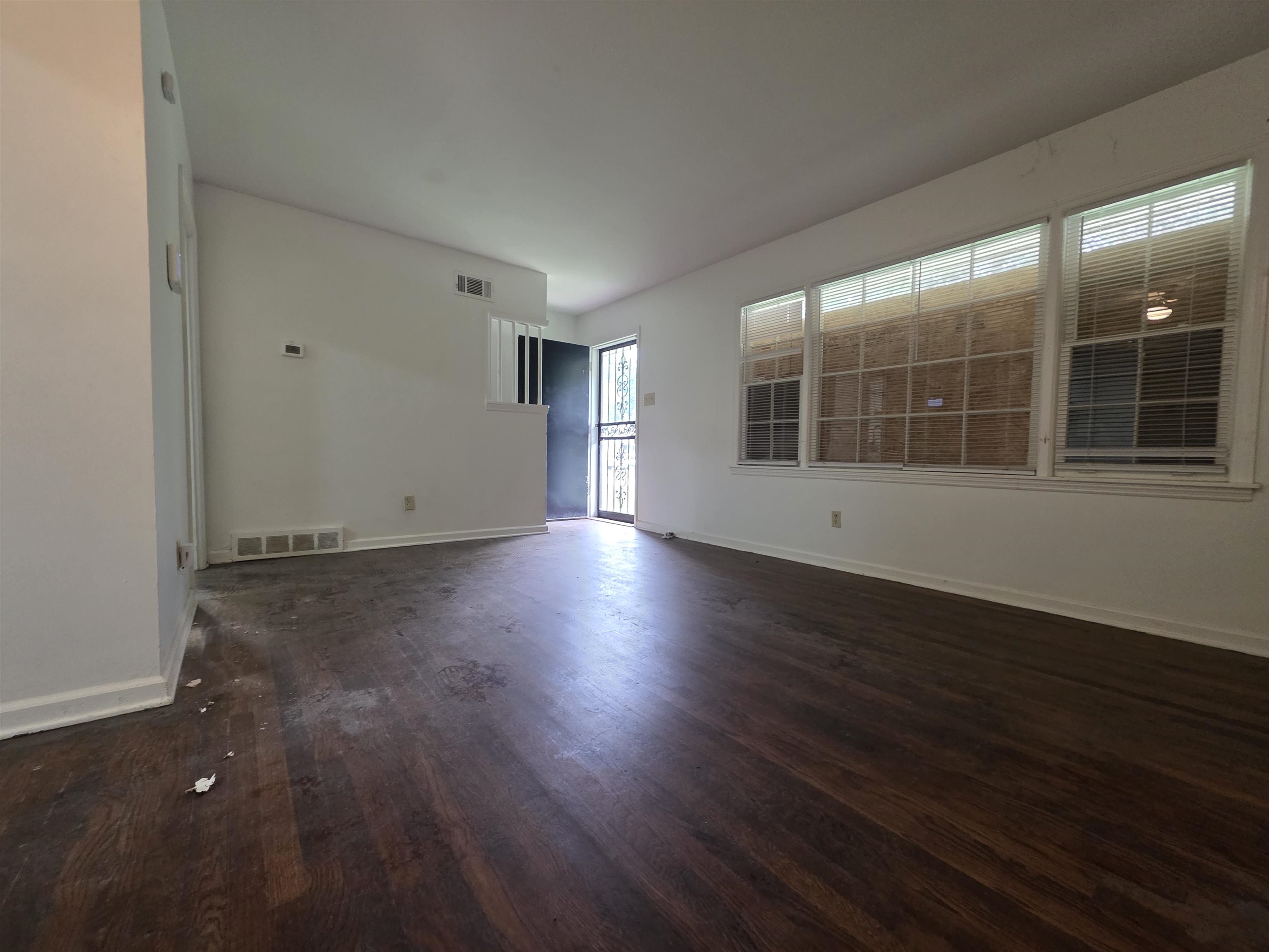 Interior room featuring wood-finish flooring, white baseboards, and multiple windows with blinds