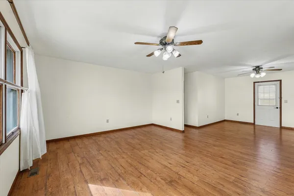 an empty room with wooden floor fan and windows