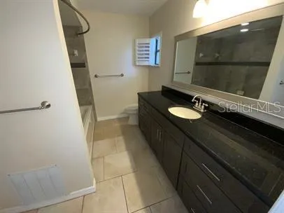 a bathroom with a granite countertop sink a toilet a mirror and vanity