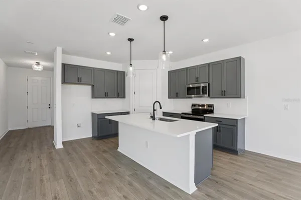 a kitchen with stainless steel appliances a stove top oven a sink a refrigerator white cabinets and wooden floor