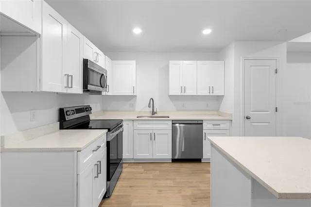 a kitchen with stainless steel appliances granite countertop a stove top oven a sink a refrigerator and white cabinets