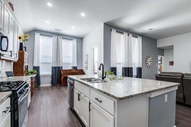 a kitchen with stainless steel appliances granite countertop a stove a sink dishwasher and a refrigerator with wooden floor