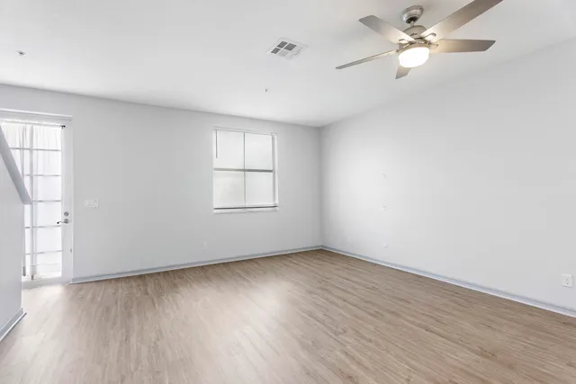 an empty room with wooden floor fan and windows