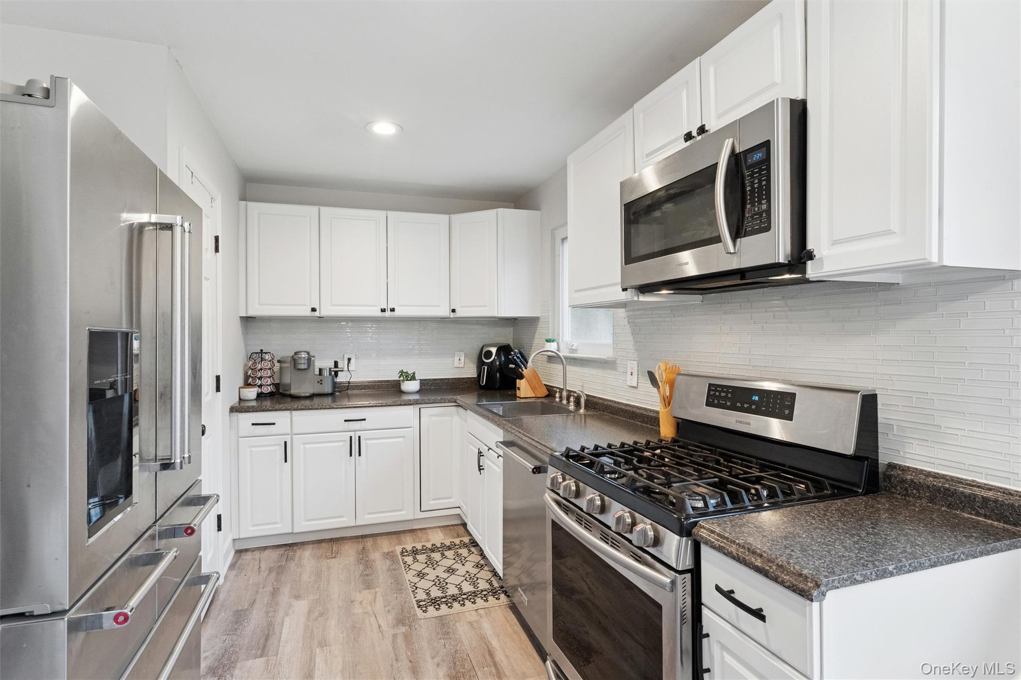 31 Howell Place Speonk, NY 11972 - Photo 11 of 16 Kitchen with stainless steel appliances, white cabinets, light wood finished floors, decorative backsplash, and recessed lighting