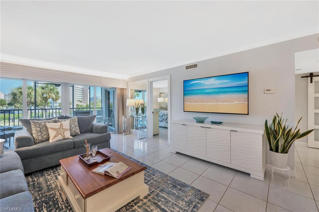 12945 Vanderbilt Drive, Unit 304 Naples, FL 34110 - Photo 19 of 45 a living room with furniture flat screen tv and a floor to ceiling window