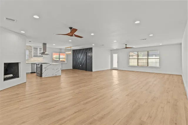a view of an empty room with wooden floor and a kitchen