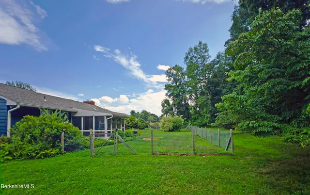 a view of a white house in front of a big yard with plants and large trees
