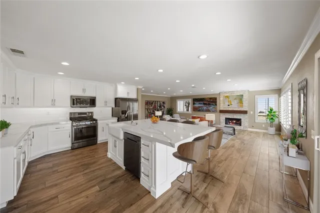a kitchen with stainless steel appliances kitchen island granite countertop a stove top oven a sink a dining table and chairs with wooden floor