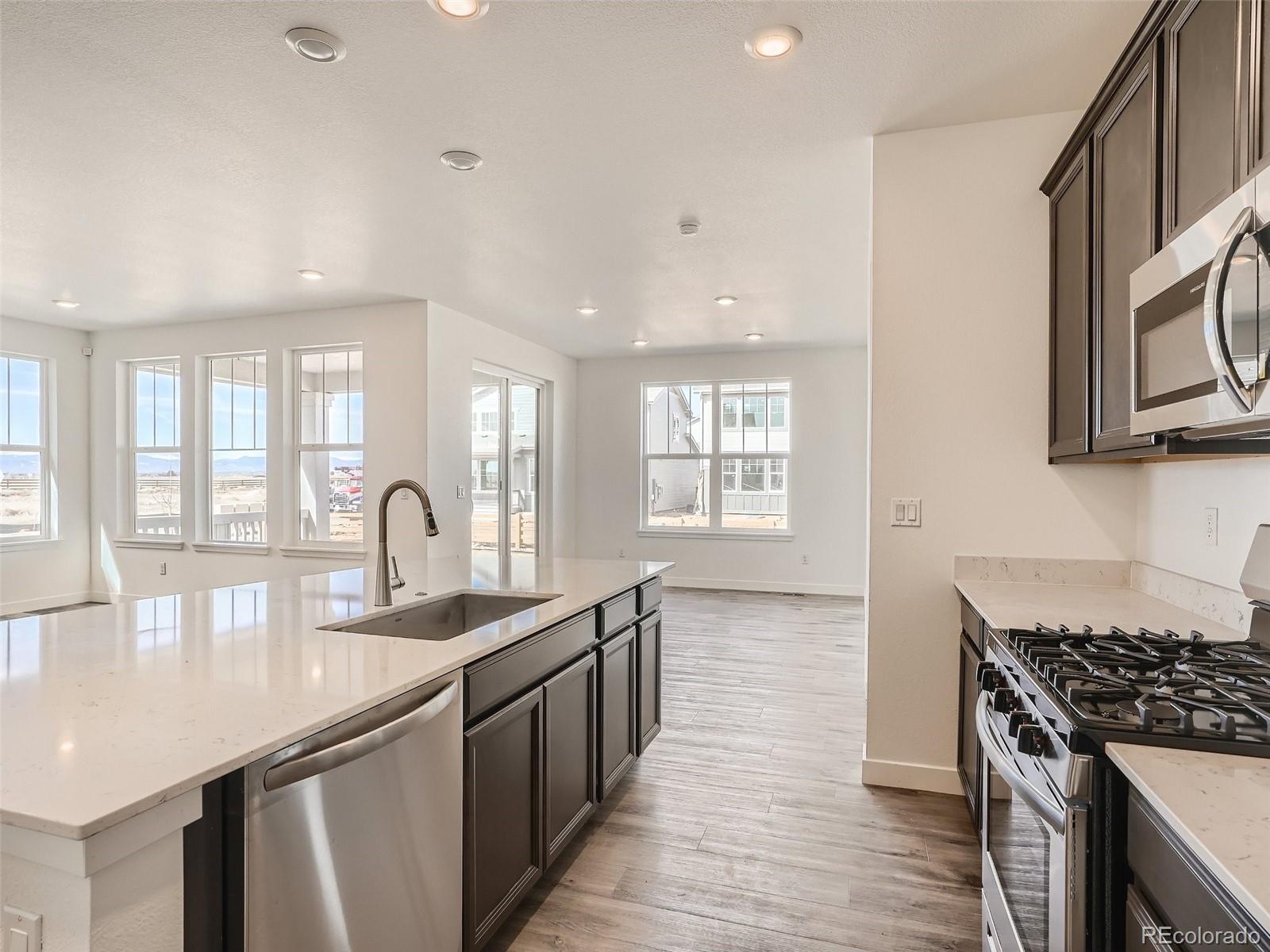 9975 Uvalda Street Commerce City, CO 80022 - Photo 12 of 29 a kitchen with granite countertop a stove a sink dishwasher and a microwave oven with wooden floor