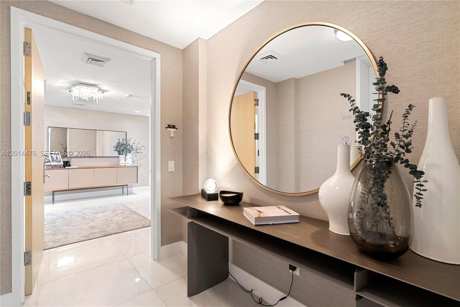 360 Ocean Drive, Unit 1106S Key Biscayne, FL 33149 - Photo 2 of 67 Entry Foyer – A refined entryway sets the tone with textured wallcovering, glossy marble-look flooring, and a sleek console with a statement round mirror. The open view into the main living area creates an inviting sense of flow.