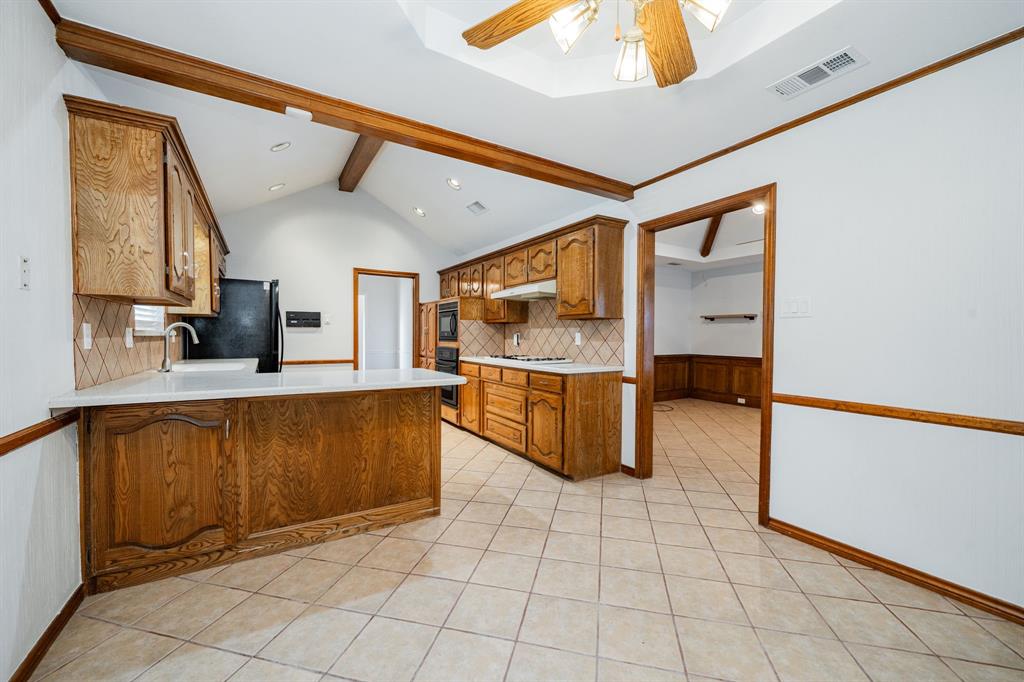 8304 Navigation Drive Rowlett, TX 75088 - Photo 15 of 40 Kitchen with tasteful backsplash, light countertops, a peninsula, brown cabinetry, and light tile patterned floors