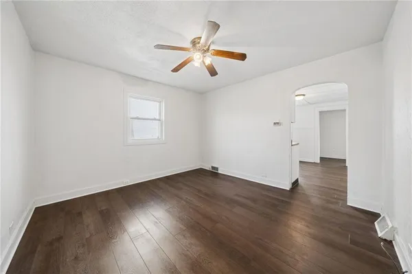 an empty room with wooden floor chandelier fan and windows