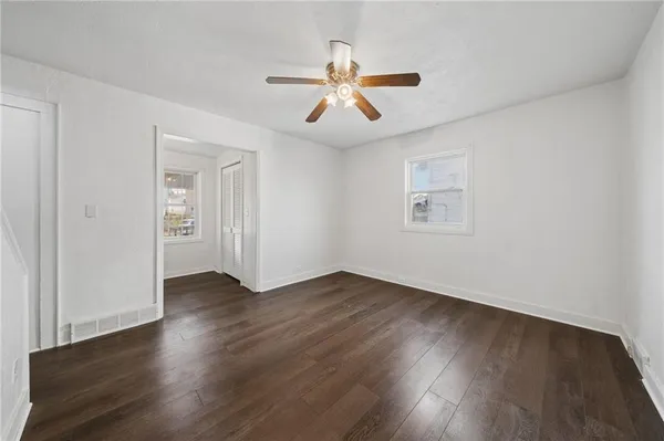 an empty room with wooden floor ceiling fan and windows