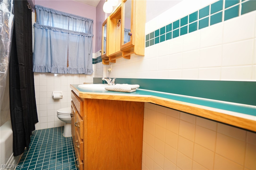453 Omar Street Struthers, OH 44471 - Photo 22 of 27 Bathroom with vanity, tile walls, dark tile patterned floors, and shower / tub combo
