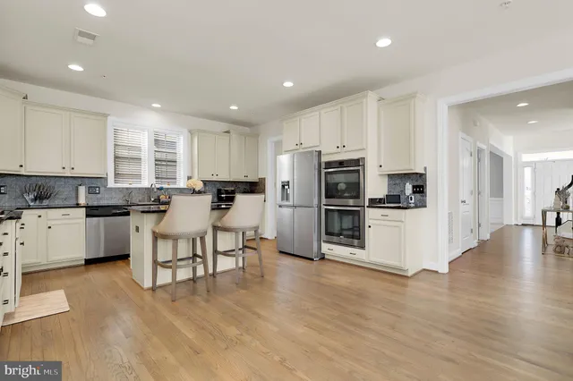 a kitchen with stainless steel appliances kitchen island granite countertop a stove a sink a refrigerator and white cabinets with wooden floor