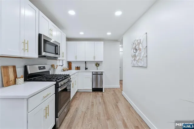 a kitchen with granite countertop a stove top oven a sink dishwasher a refrigerator white cabinets and wooden floor