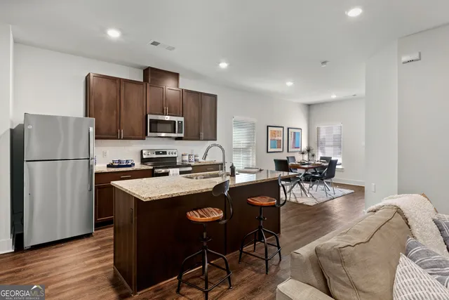 a kitchen with stainless steel appliances granite countertop a stove a refrigerator a sink a dining table and chairs