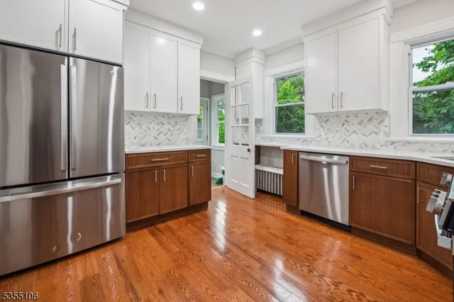 a kitchen with stainless steel appliances granite countertop a refrigerator a sink dishwasher a stove and white countertops with wooden floor