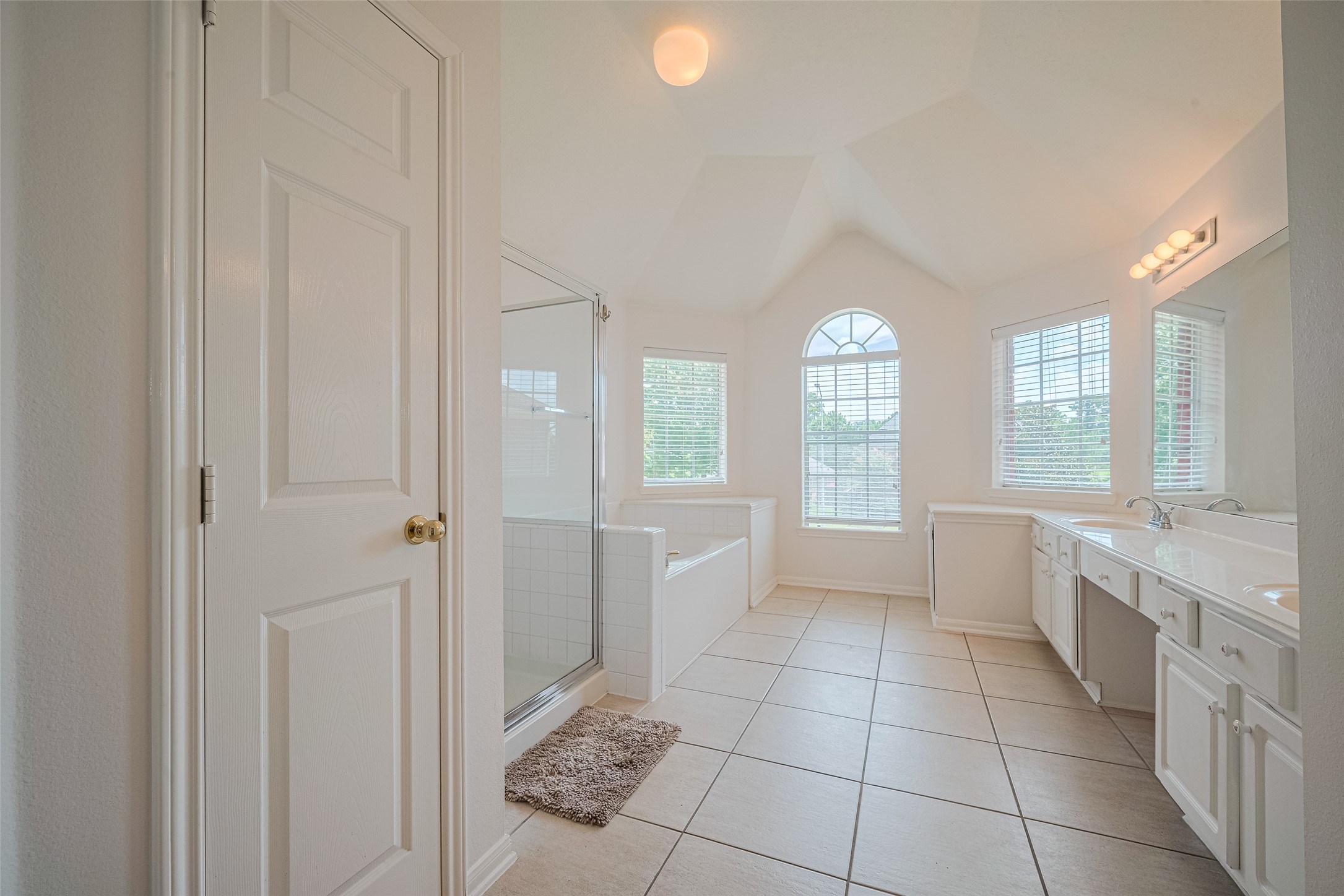 9218 Memorial Pines Way Spring, TX 77379 - Photo 28 of 39 This spacious bathroom features a vaulted ceiling, large windows for natural light, a double vanity, and a separate shower and tub area. The neutral tile flooring and white cabinetry create a bright, clean atmosphere.